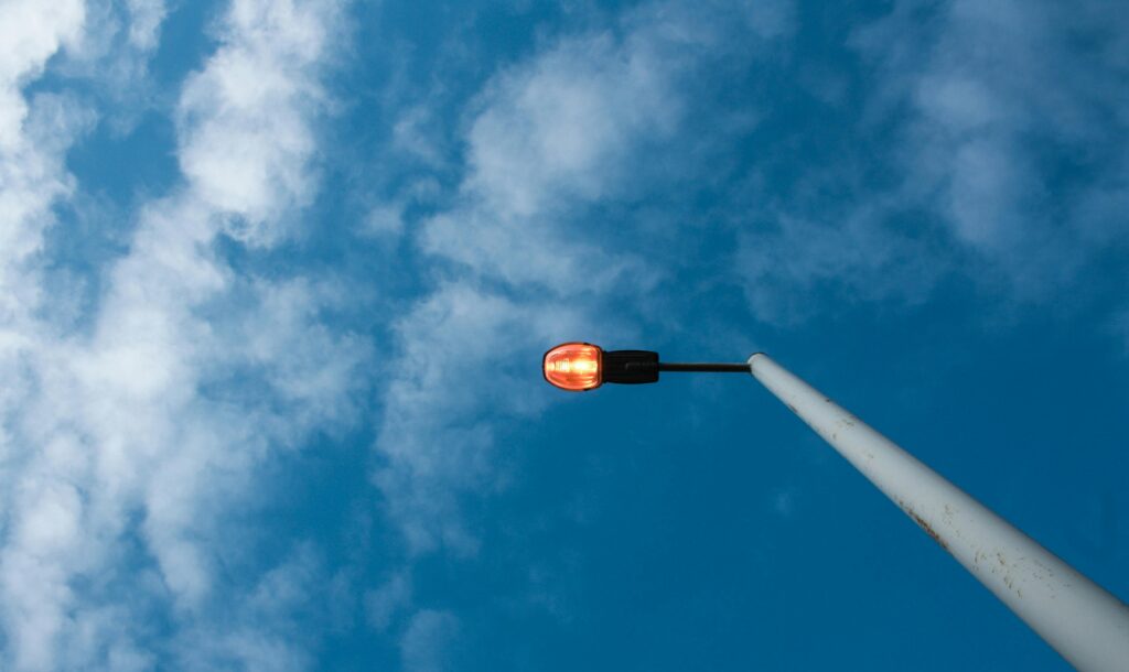 A street light against a bright blue sky with scattered clouds during daylight.
