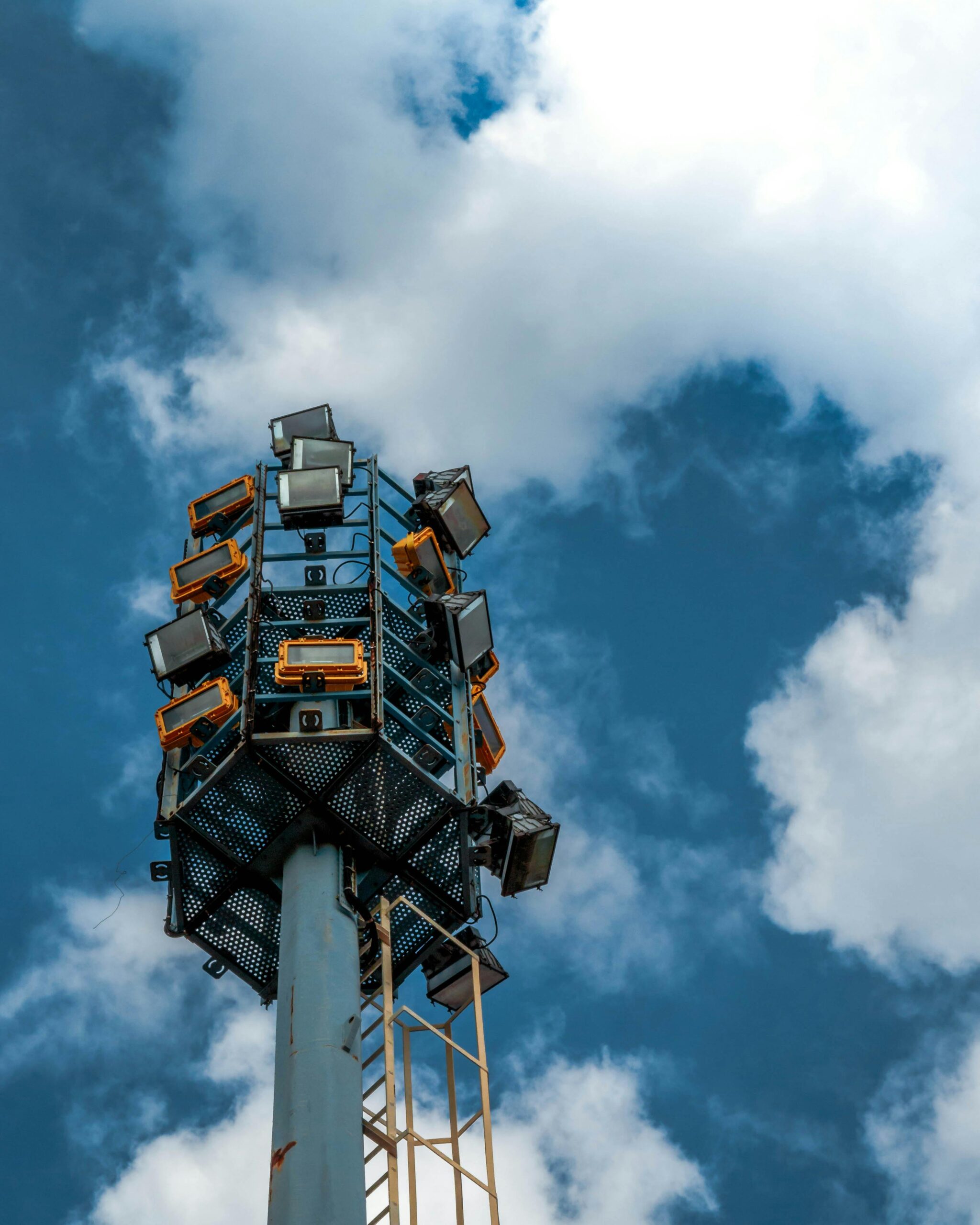 Low-angle view of spotlights on a tall pole set against a vibrant blue sky with clouds.